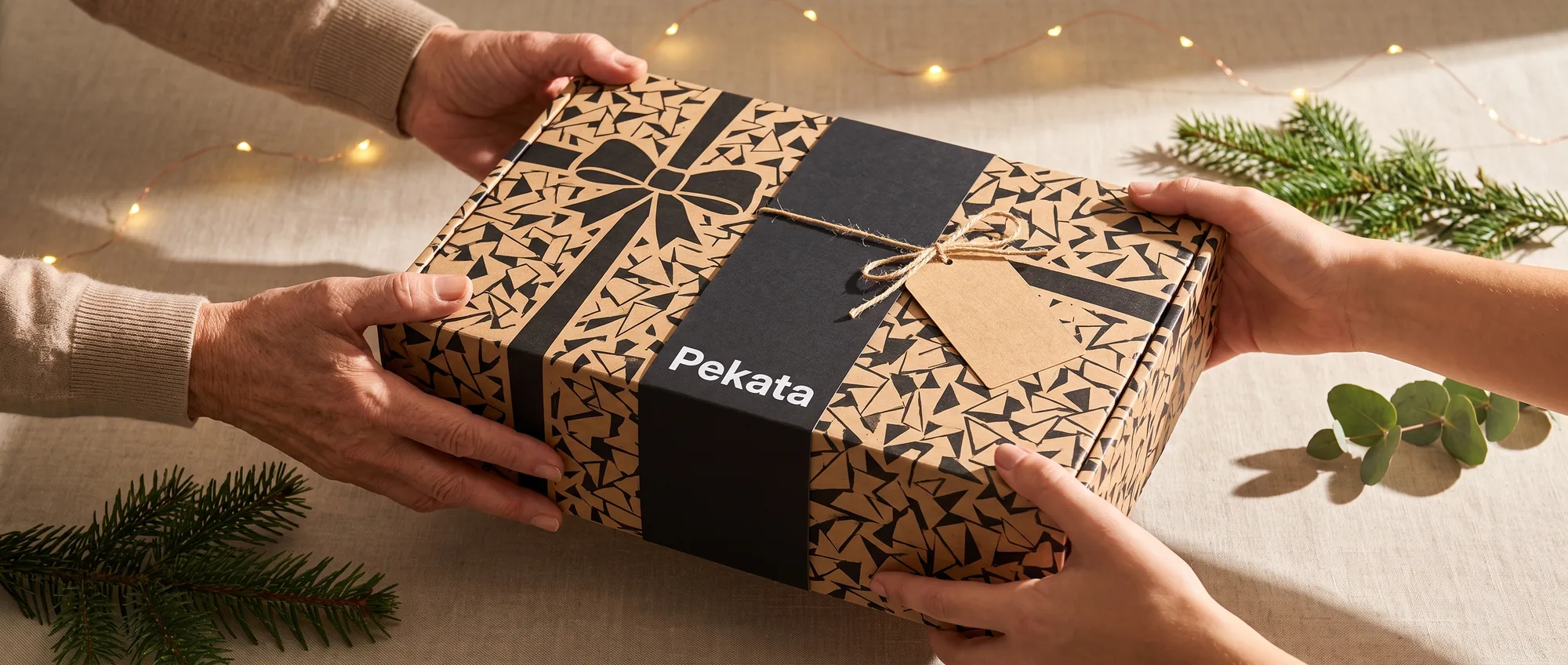 Two pairs of hands giving and receiving a Pekata gift box with kraft label and trencadís pattern